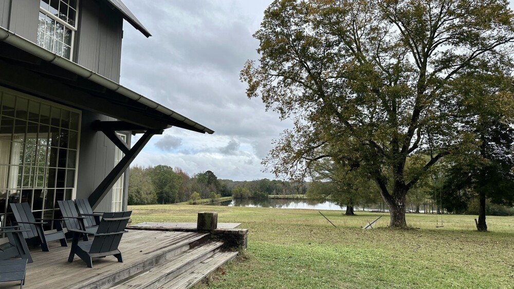 A house sits on a fam property aside a tree and a pond in the background.