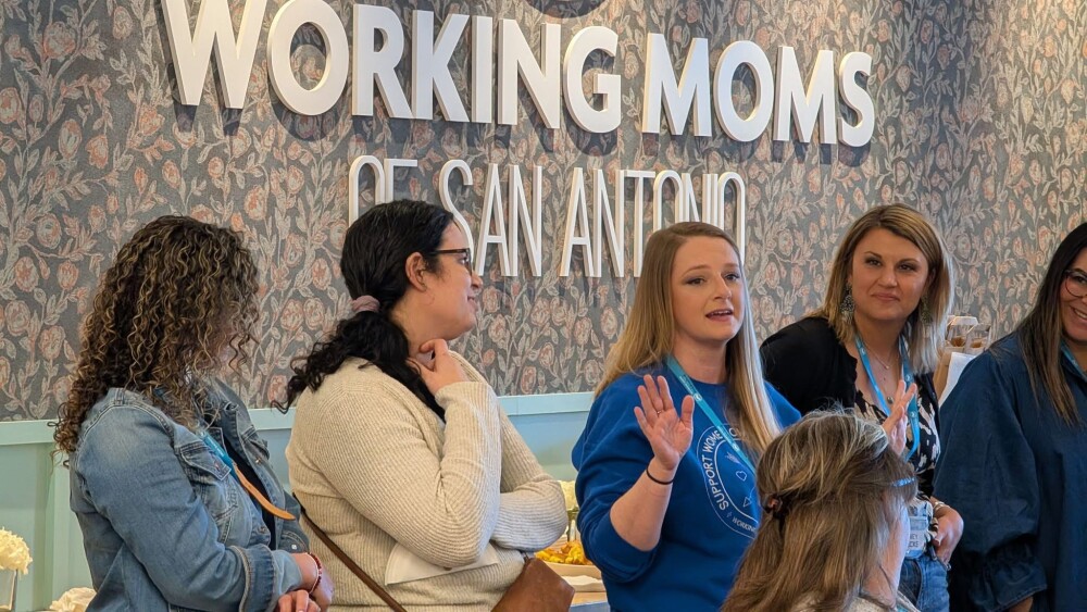 Four people stand in front of a sign that reads "Working Moms of San Antonio"