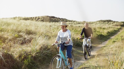 Mature couple riding bicycles on sunny beach grass path