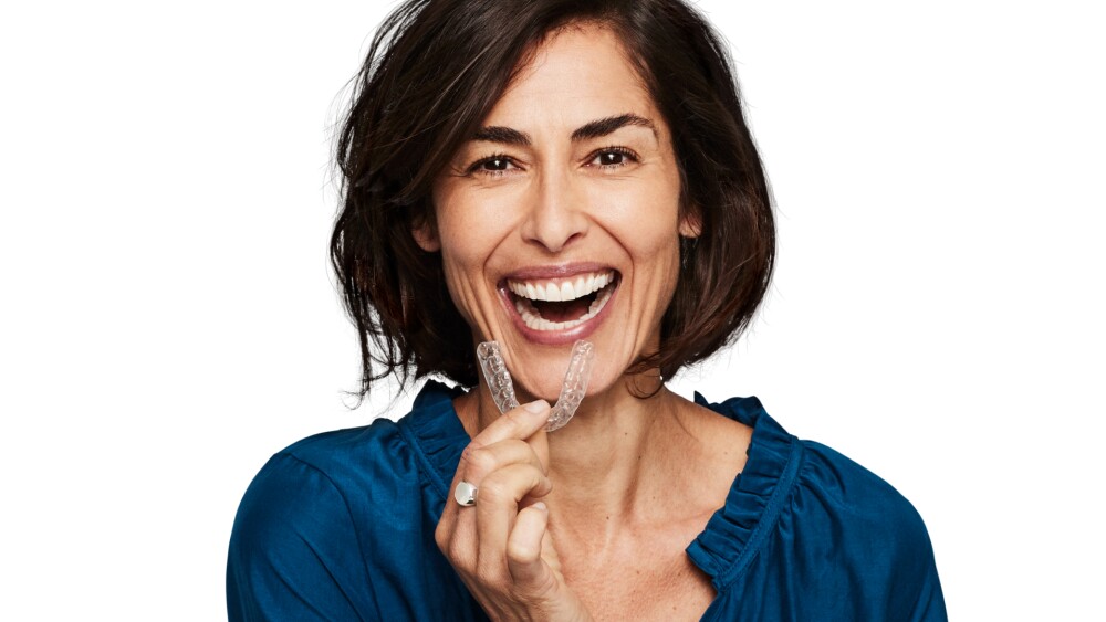 woman smiling with clear teeth aligner in her hand