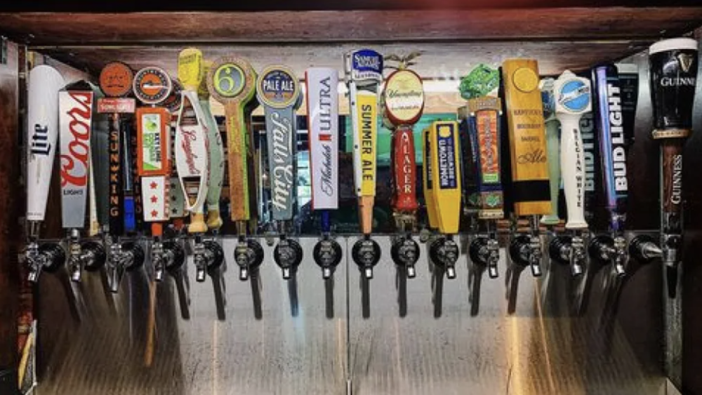 The image shows 16 different beer tap handles on a bar.
