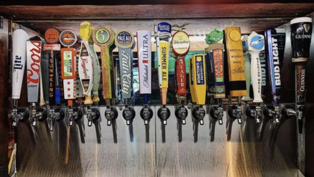 The image shows 16 different beer tap handles on a bar. 