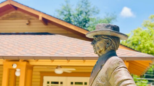 A sculpture of Frank Lloyd Wright wearing a wide-brimmed hat stands in front of the Sharp Family Tourism and Education Center