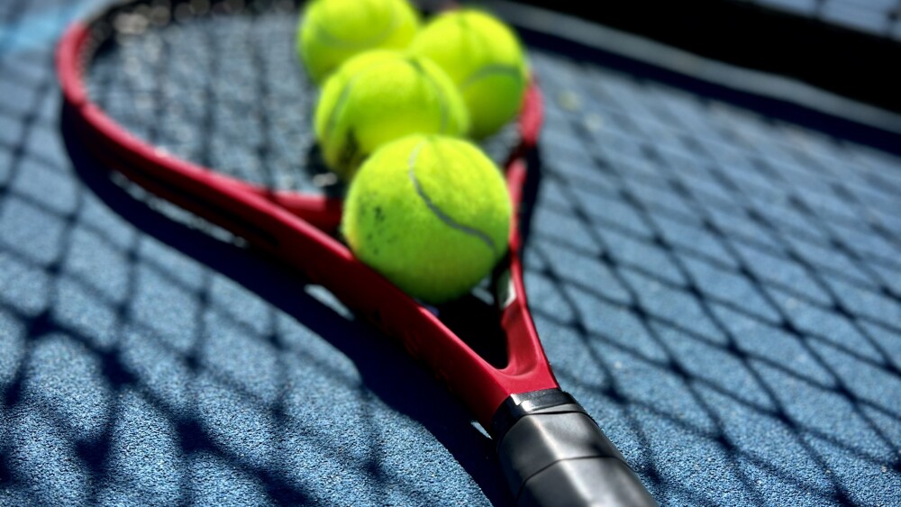 A tennis racket and tennis ball beneath a net on a tennis court.