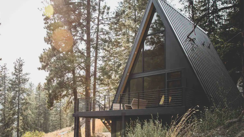 An A-frame cabin painted black with tall windows, surrounded by forest.