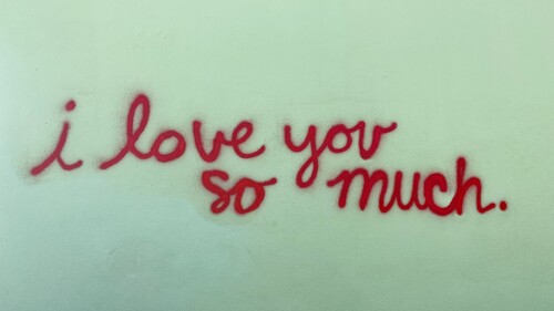 "I Love You So Much" spraypainted in red cursive on a green wall.