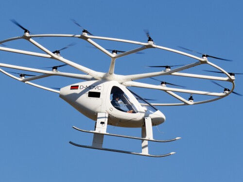 The air taxi sits outside Volocopter HQ. It is a white vehicle and resembles a two person drone.
