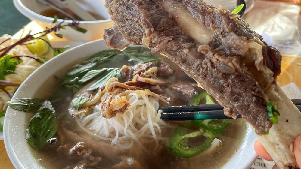 Someone holds a beef bone in front of their bowl of pho.