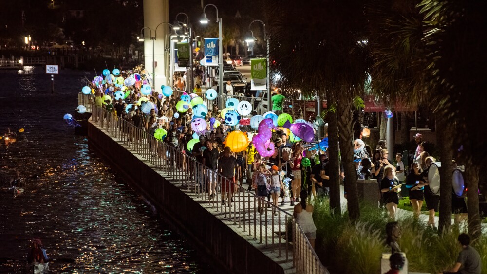 People hold lit lanterns along the river.