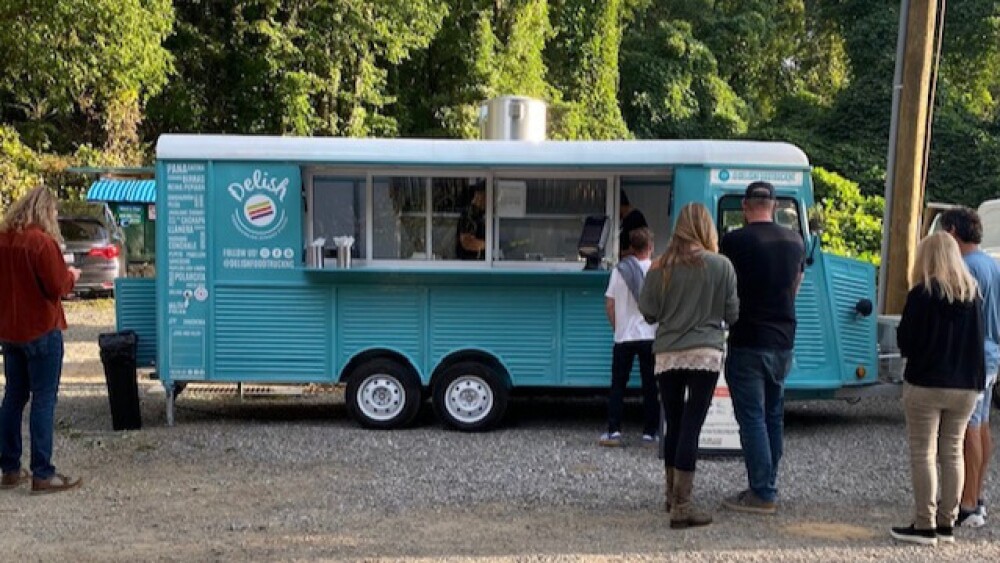 Blue food truck with people waiting outside.