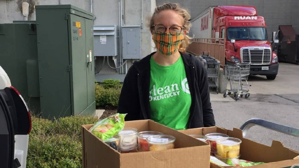 A woman wearing a Glean Kentucky shirt in front of boxes with produce.