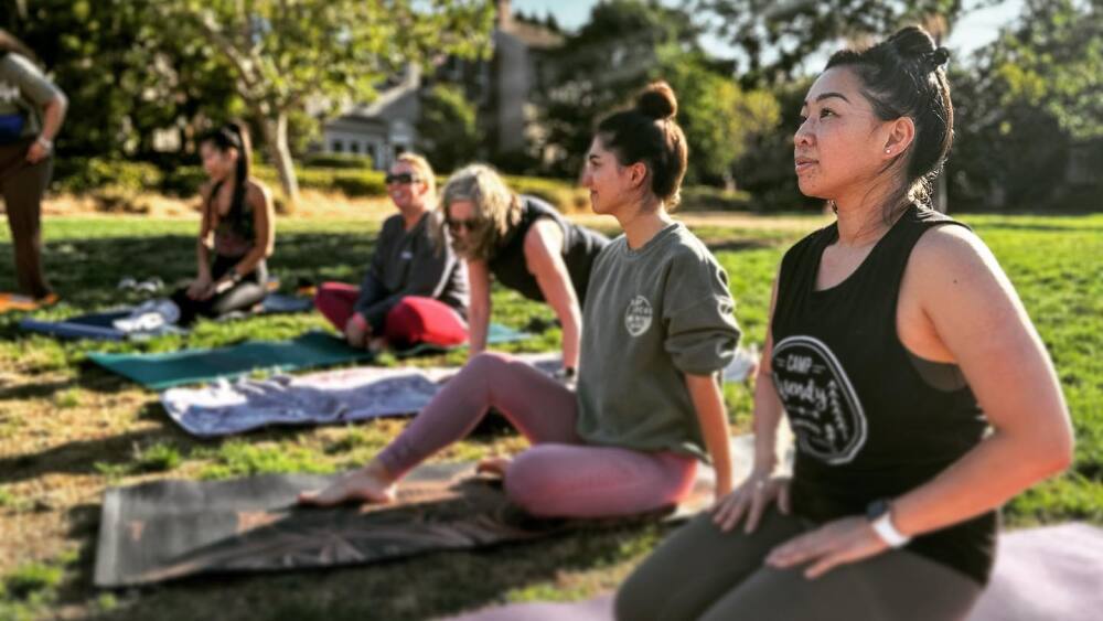 Women sit on yoga mats in a park.