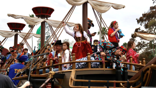 Children aboard a Gasparilla pirate ship float. They are throwing beads into the crowd, dressed like pirates.