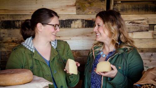 Two women at Landmark Creamery smile at each other holding wedges of cheese.jpeg