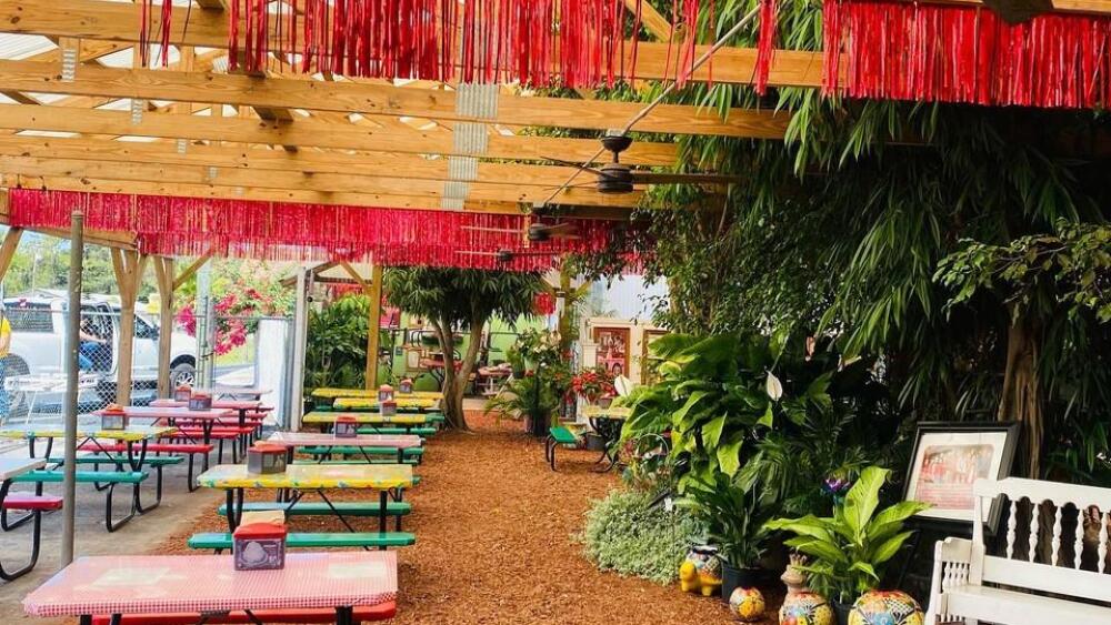 An outdoor area covered by wooden beams that features rows of colorful picnic tables.