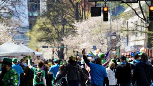 A crowd of people wave while taking part in the St. Patrick's Day parade in Uptown.