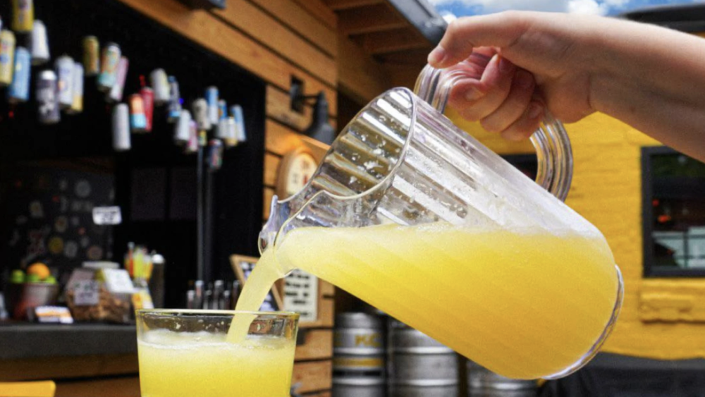 A pitcher of mimosas pouring into a glass outside in a beer garden.