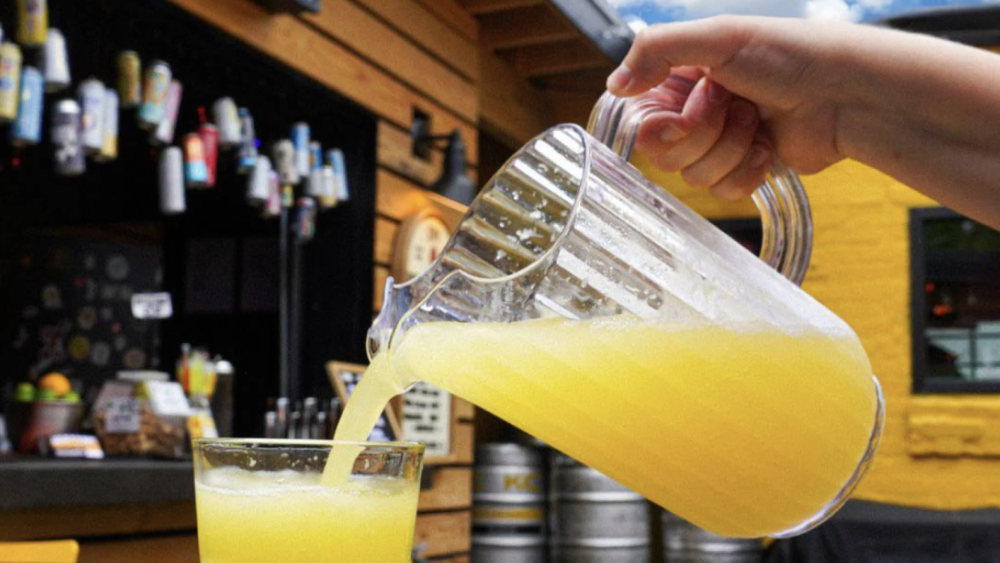 A pitcher of mimosas pouring into a glass outside in a beer garden. 