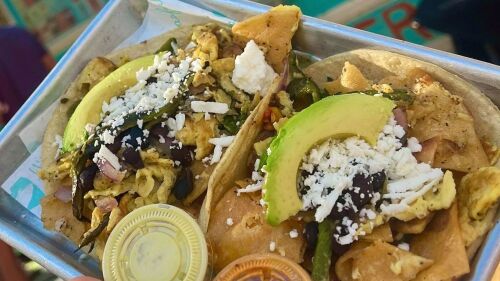 Two tacos topped with crumbled cheese, avocado, and beans. 