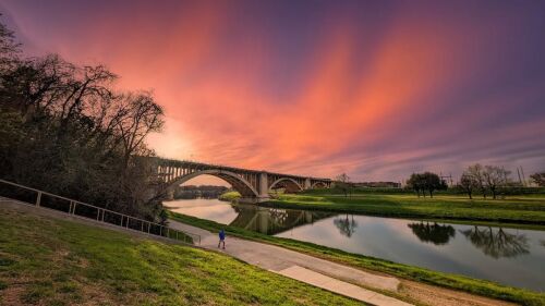 An orange and purple sunset over a river and bridge.