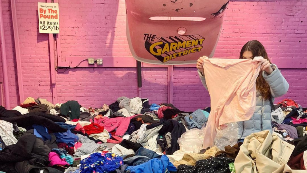 Person holding up a shirt in a pile of clothing on the floor