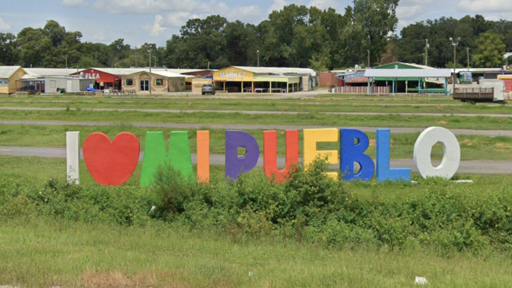 A colorful sign reading "I love Mi Pueblo" in the foreground with flea market buildings in the background