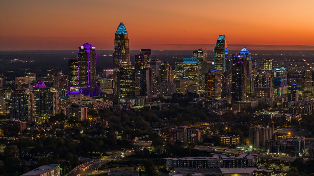 The Charlotte skyline at dusk with an orange sunset in the background of several tall buildings lit up.