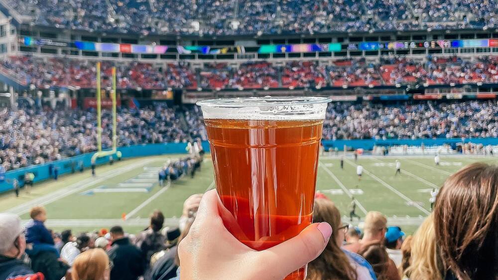Someone holds a beer up in the Nissan Stadium stands as the game is happening on the field.