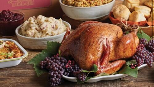 A Thanksgiving meal sits on a wooden table. There is a turkey, roasted potatoes, stuffing, and other food items.