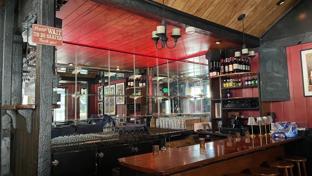 An interior shot of the new Cheese Room shows a very cozy red and black aesthetic with wooden features and wine already stocked on a shelf.