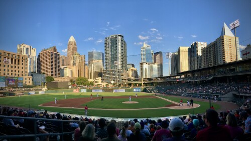A skyline shot of Uptown Charlotte over a crowd watching baseball inside a stadium.
