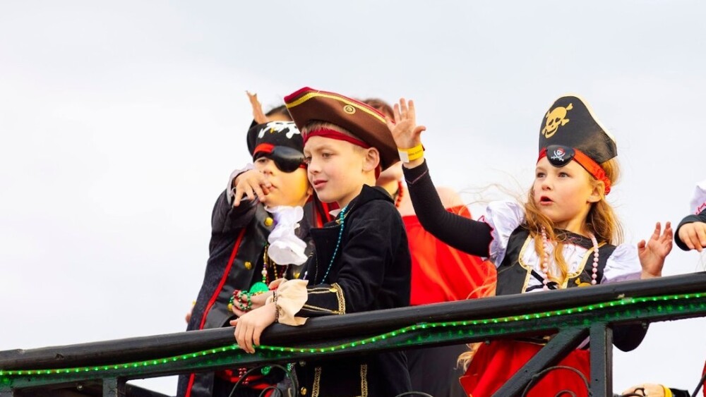 Three little kids dressed as pirates toss beads down to onlookers off of a float.