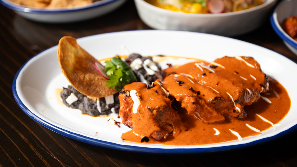 A dish of sliced pork loin medalions with bright red mole sauce.