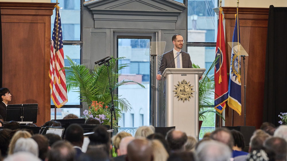Nashville mayor Freddie O'Connell speaks at a podium during a formal event, with flags and an audience visible in the background.