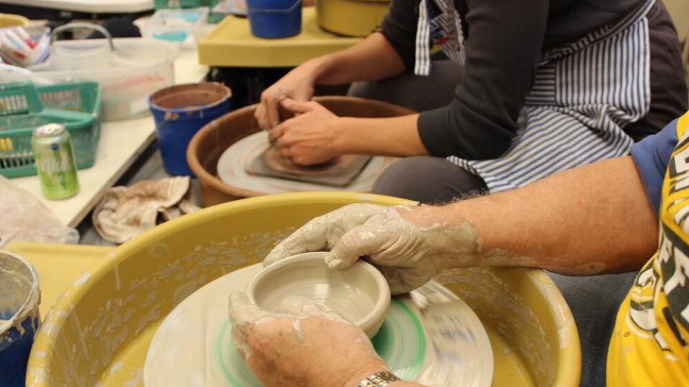 An photo of two people at a pottery classes with only their arms visible.