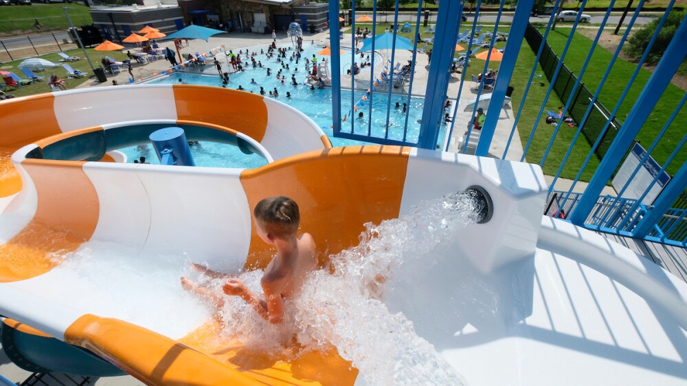 A young boy sliding down an orange and white striped water slide.