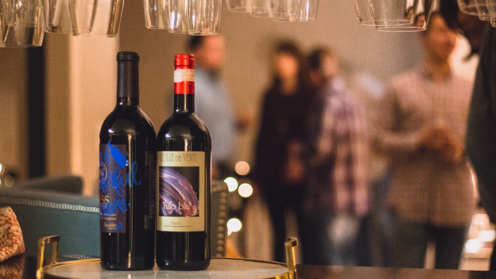 Two bottles of wine sit on the counter as dinner guests mill about in the background.