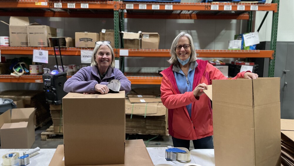 Two ladies taping up boxes smiling