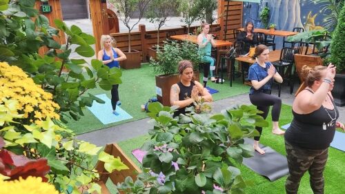 Women doing a stork pose during a yoga class outdoors.