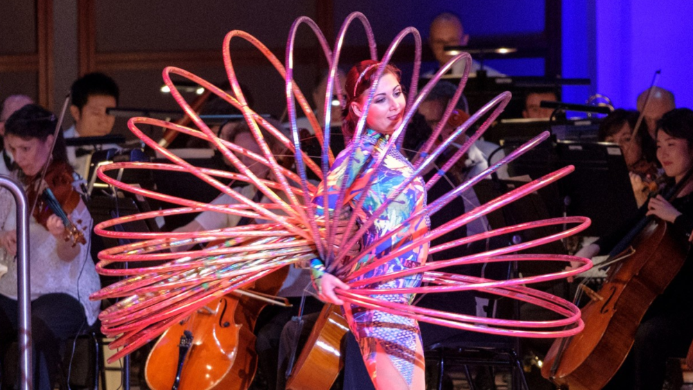 A performer holds a dozen or so hula hoops while standing in front of members of the NC Symphony.