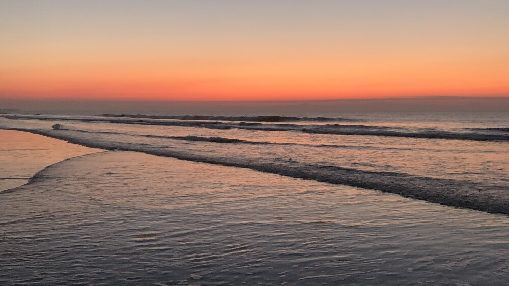 This photo shows a bright orange sunrise over the calm waves on IOP.