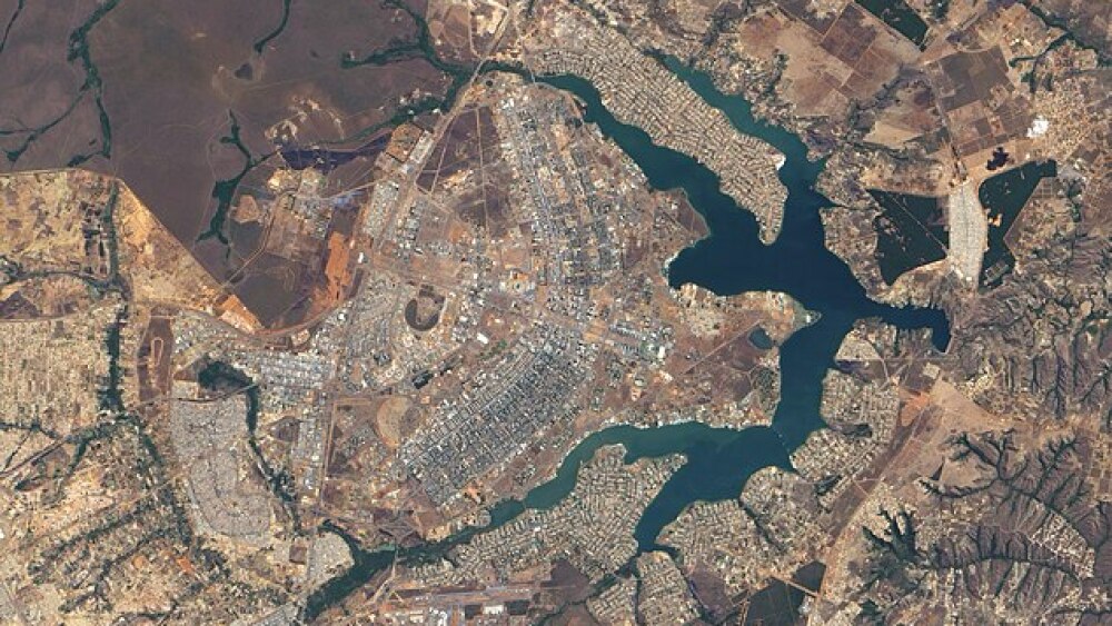 An aerial shot of Brasilia where the blue lake surrounds buildings in the rough shape of an airplane.