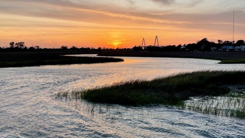 The light from the sunset reflects off Shem Creek, while the sky fades from a fire orange to pale blue.