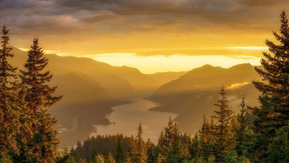 Steep cliffs and forested hills rise up along both sides of the Columbia River as the sun hangs low in the sky.