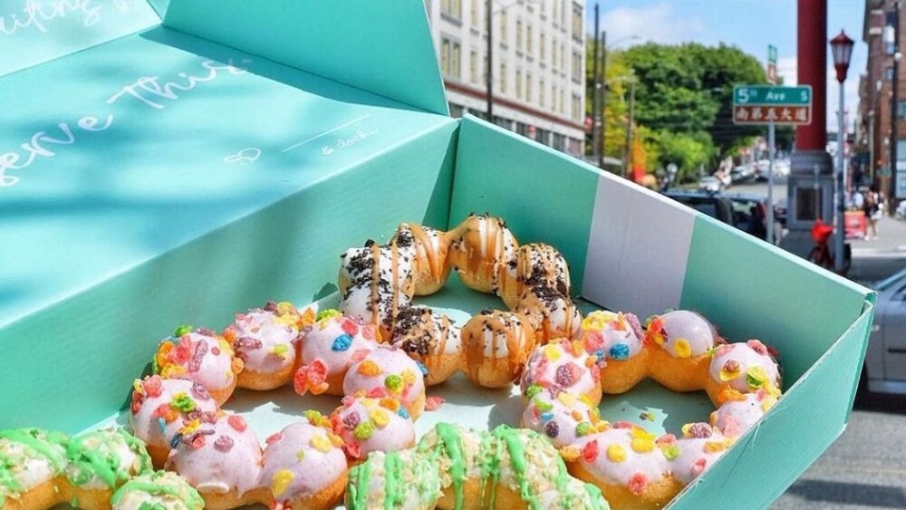 A light blue box filled with colorful, cereal-topped mochi doughnuts.
