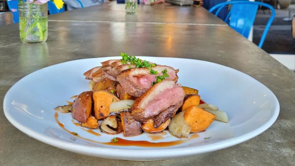 A photo outside of Plates Kitchen of Cast Iron Duck with duck breast, sweet potatoes, rhubarb, charred onions, and port + red wine gastrique.