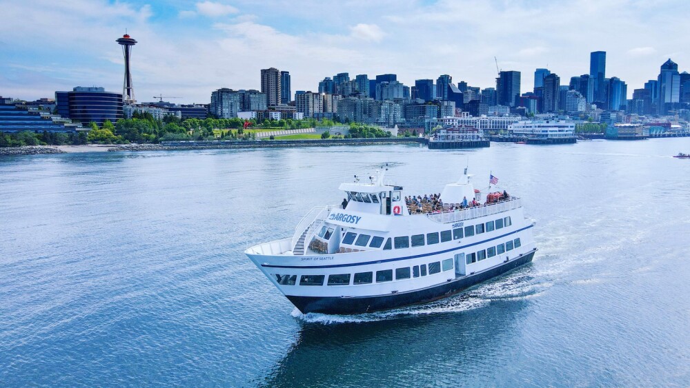 An Argosy cruise ship is pictured while on one of its boat tours past the Olympic Sculpture garden. The green grass and trees key in that this was taken during a beautiful summer day.