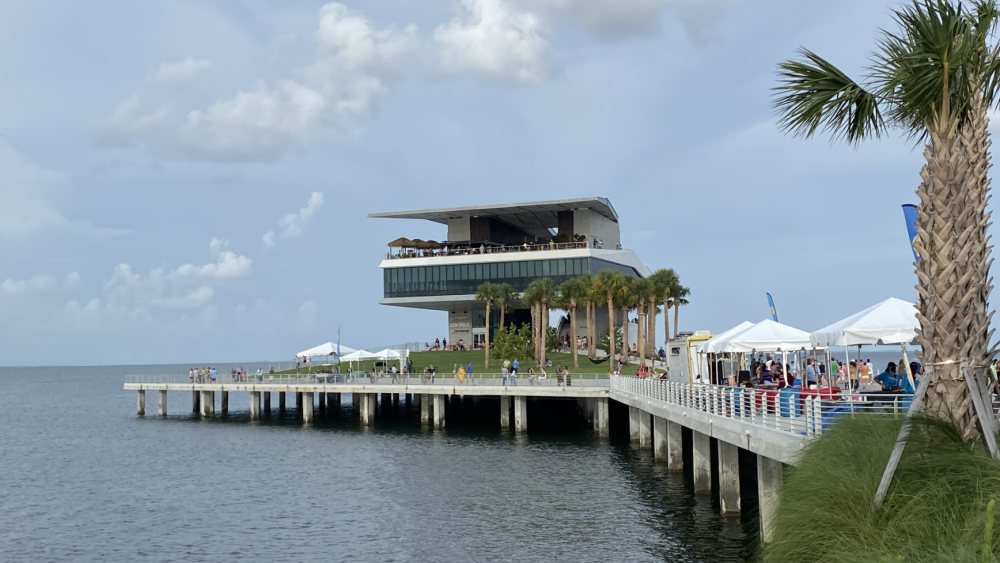 The St. Pete Pier juts out over bluey grey skies. There are people walking around.