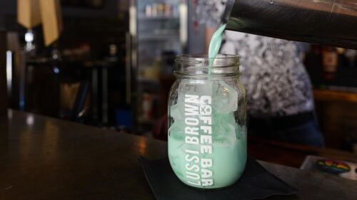 Barista pours an iced drink into a glass.