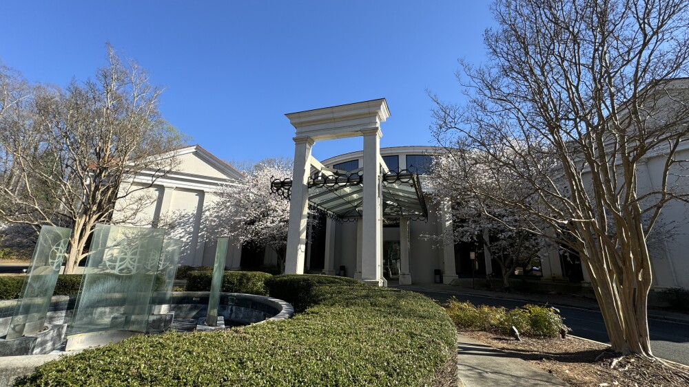 The pillared archway of a white museum building, surrounded by greenery and trees.